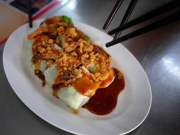 istock Southern Thai food, fresh Rice sheet Spring rolls, cold rolls topping with crackling, served with special sweet brown gravy, served in white oval shape plate 1427256567