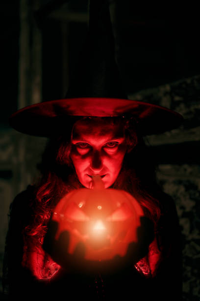 spooky witch with glowing pumpkin looking at camera on halloween portrait