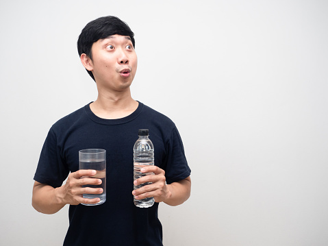 Asian man holding glass with water bottle feels excited looking at copy space