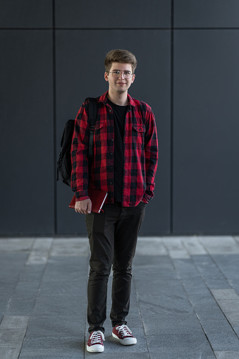 Portrait of teenage male student standing wall in corridor of a college. Caucasian male student in university campus.