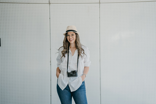 Portrait of young female photographer standing against white background