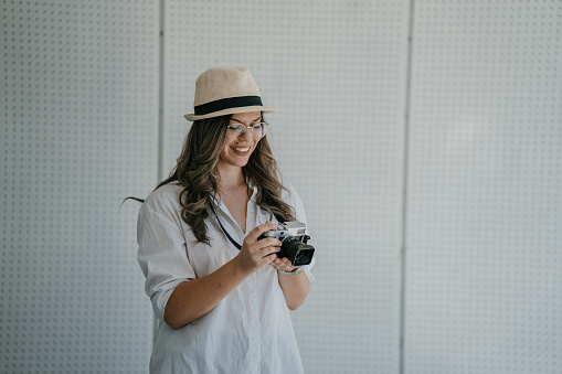 Beautiful young woman with retro camera standing against white background outdoors on sunny day