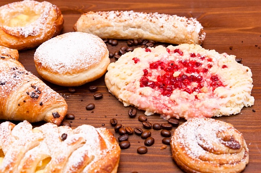 Delicious filled croissants, apple strudel, cinnamon roll and Danish pastries with vanilla pudding and currants on a retail display of a bakery, decorated with coffee beans. This image is part of a series.