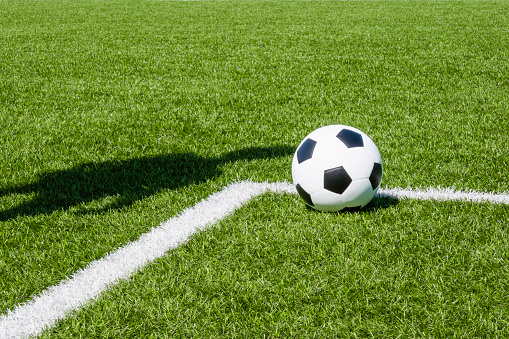 Soccer football sport background. Soccer ball and shadow of player on artificial turf soccer field in sunny day outdoors.