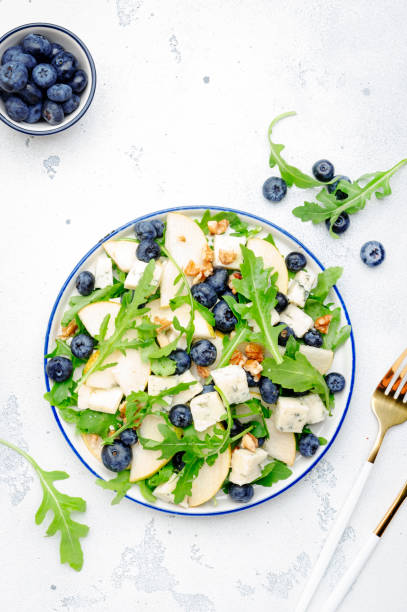 istock Delicious arugula salad with pears, blueberries, roquefort cheese and walnuts. Black kitchen table background, top view 1427276275