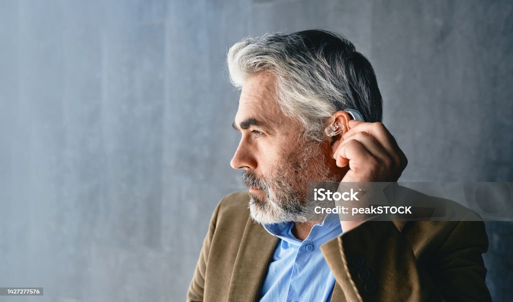 Grey-haired mature man with hearing impairment using hearing aid. Hearing solutions for deafness people Hearing Aid Stock Photo