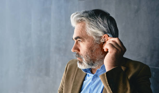 Grey-haired mature man with hearing impairment using hearing aid. Hearing solutions for deafness people Grey-haired mature man with hearing impairment using hearing aid. Hearing solutions for deafness people HEARING AID stock pictures, royalty-free photos & images