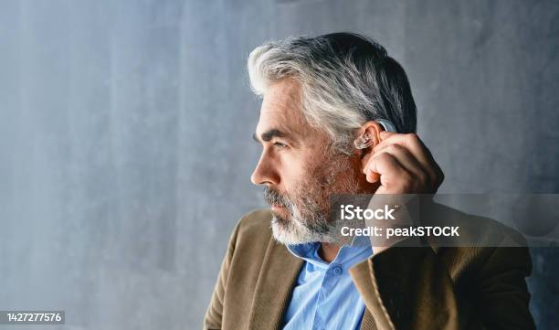 Greyhaired Mature Man With Hearing Impairment Using Hearing Aid Hearing Solutions For Deafness People Stock Photo - Download Image Now