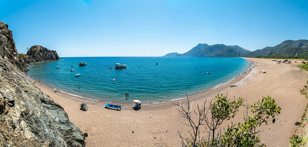 Cirali, Antalya, Turkey - August 17, 2021. Panoramic view of sand beach in Cirali hamlet of Antalya province in Turkey. View with people and boats in summer.
