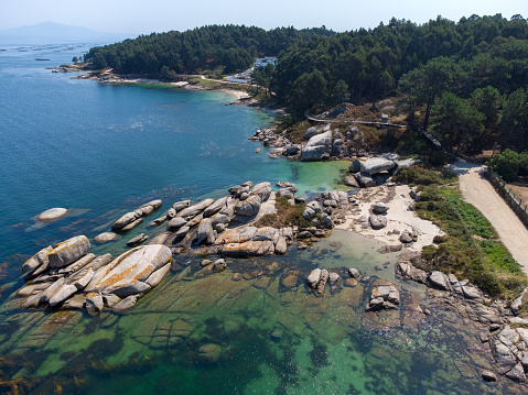 aerial dron view of a small beach with white sand and transparent turquoise water surrounded by rocks in Illa de Arousa, Galicia, Spain. With Copy Space