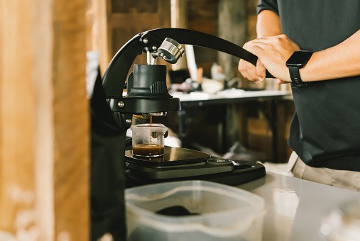 A barista using the Flair Espresso Maker is a non-electric coffee brewing device using a lever or handle. For extracting espresso on a table with coffee making iced coffee. soft focus