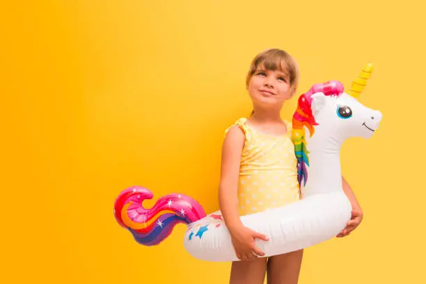 Photo of child girl in swimming suit  with unicorn shaped inflatable ring against a yellow background. copy space