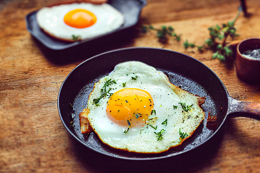 fried eggs, scrambled eggs in a frying pan with seasonings and spices, on a wooden table, close-up, rustic style, farm