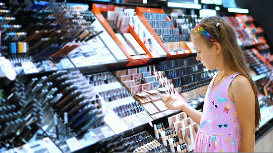 cosmetics shop, pretty girl, kid, carefully considers cosmetic products, in beauty store. Little fashion-girl. High quality photo