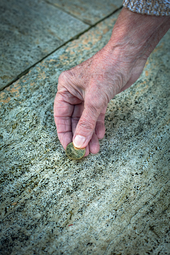 close-up of old womans hand picking up a coin from the floor