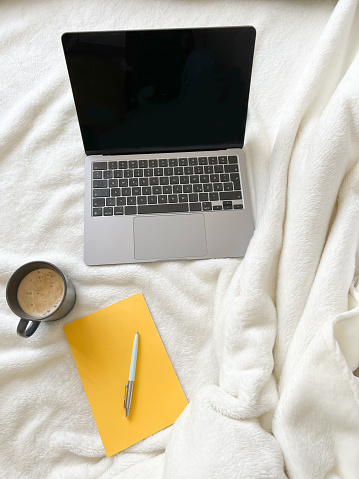 notebook, coffee and notepad on white blanket in the bedroom