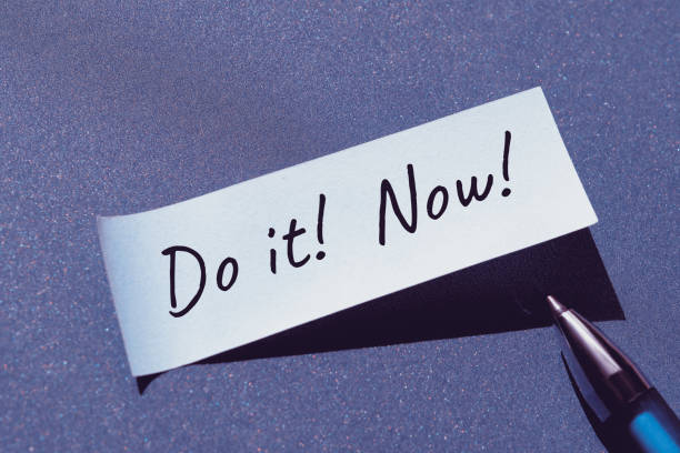 istock Do it now motivator message written on post it note, sticky paper with pen. Single simple minimal motivation note stiker on blue paper background. 1427286573