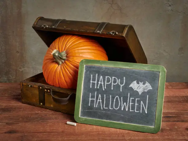 Happy Halloween blackboard sign with a large pumpkin in a small retro suitcase, greeting card