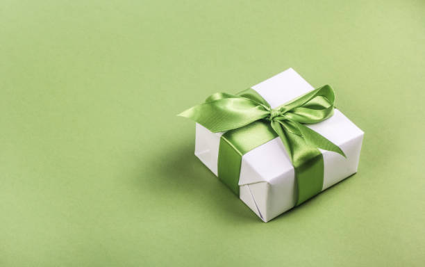 White gift box with green bow on green background. Gift box copy space stock photo