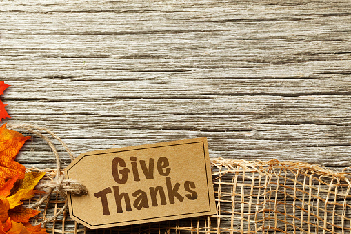 A tag labeled Give Thanks is  attached to a rustic piece of burlap resting on a textured wood plank.