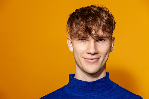 Close up studio portrait of a caucasian young man in a blue longsleeve on a yellow background
