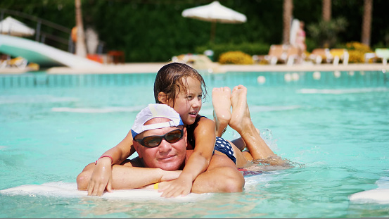 man in sun glasses, father and daughter, kid girl, playing in the pool water, having fun together. Happy family relaxing by the swimming pool on a hot summer day at water park. Summer vacation concept. High quality photo
