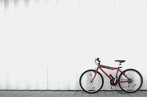 Red mountain bike alone without people leaning against a white wall and with space for text on top.