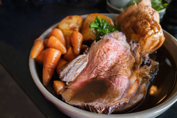 fatias de rosbife em um prato com cenouras, batatas assadas, um pudim de yorkshire e molho, fazendo uma refeição assada completa de domingo. - yorkshire pudding - fotografias e filmes do acervo