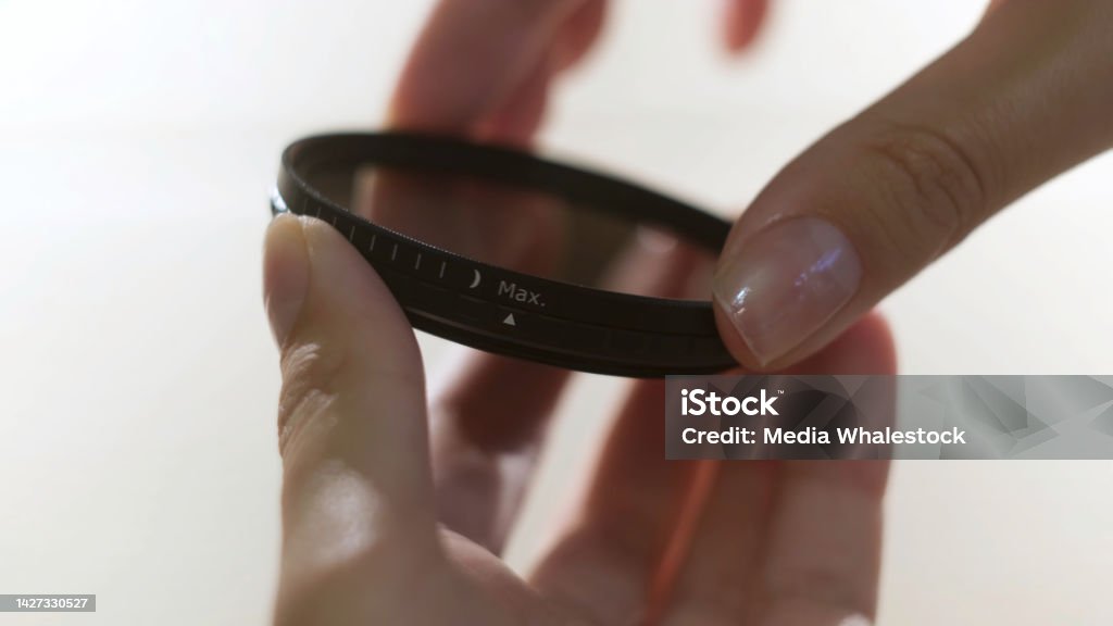 Close up of polarizing lens filter in girls hands isolated on white background. Concept. Woman turning into the both sides mechanism of lens filter. Close up of polarizing lens filter in girls hands isolated on white background. Woman turning into the both sides mechanism of lens filter. Lighting Technique Stock Photo