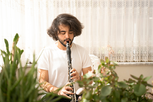 young long-haired boy playing a woodwind instrument at home.