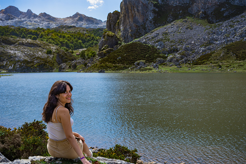 portrait of a young woman sitting on the rocks on the shore of one of the lakes of covadonga (asturias,Spain) with space for copy.