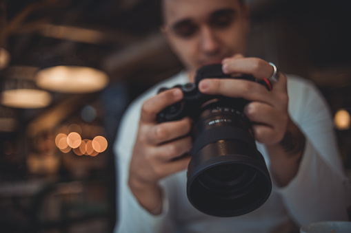 A young man is sitting in a coffee shop and using his digital camera