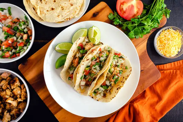 Three tacos on a plate surrounded with toppings and tortillas