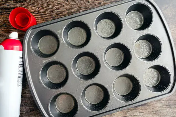 Greased non-stick muffin pan with an aerosol bottle of cooking spray