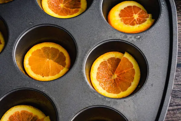 Greased muffin pan with thin slices of orange in each cup