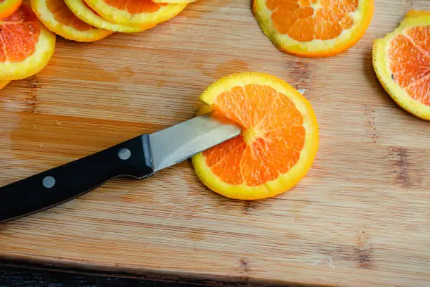 Thinly sliced orange on a bamboo cutting board with a kitchen knife