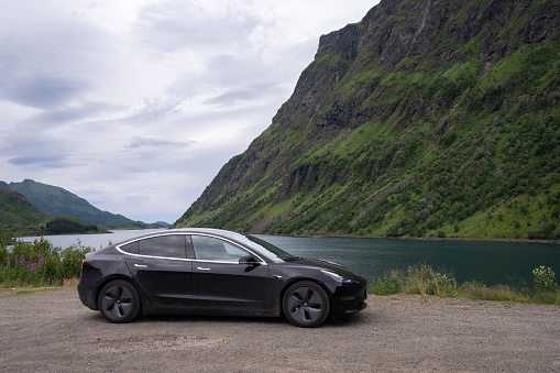Husjord, Norway - July 20, 2022: Lofoten scenic view. A static shot of a solid black Tesla Model 3 dual motor with tinted windows and aero wheels at Husjord, Lofoten Islands. Selective focus