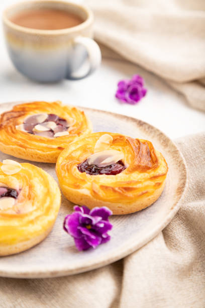 istock Small cheesecakes with jam and almonds with cup of coffee on a white concrete background. Side view, selective focus. 1427351046