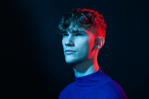 Close up studio portrait of a caucasian young man in a blue longsleeve on a black background