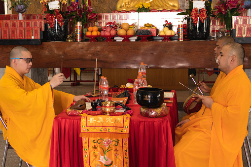 Bandung, Indonesia - January 8, 2022 : The monks with orange robes sit down in the chair while praying to the god on the altar inside the Buddha temple