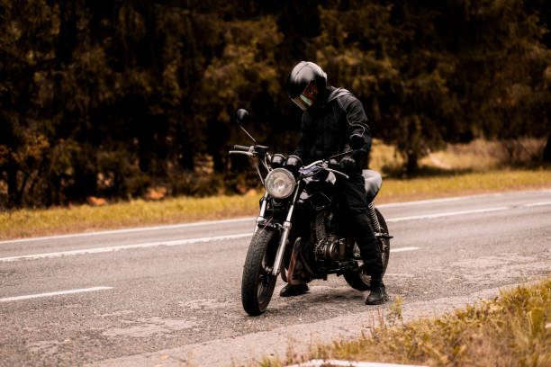 istock motorcyclist in a motorcycle jacket and a helmet with a sun visor on a custom motorcycle cafe racer. Stylish motorcyclist and autumn road. 1427369994