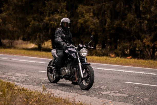 istock motorcyclist in a motorcycle jacket and a helmet with a sun visor on a custom motorcycle cafe racer. Stylish motorcyclist and autumn road. 1427370022