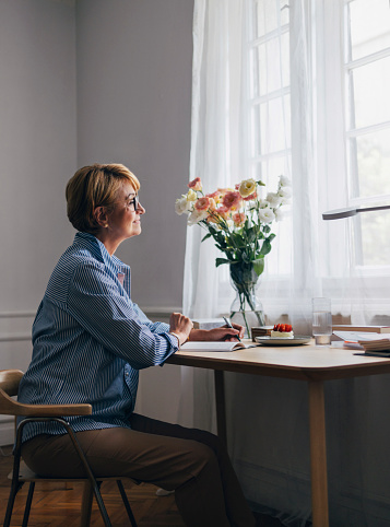 A side view of a smiling focused Caucasian female sitting at the desk and looking away while holding a pen and contemplating some ideas.