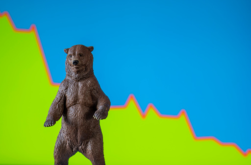 A bear standing in front of a  graph showing declining numbers representing the economic market.