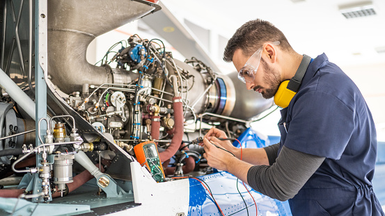 Aircraft mechanic fixing jet engine and using multimeter, mid shot. Male engineer examining helicopter, side view