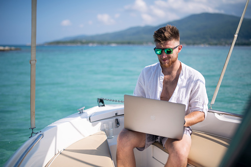 Young businessman working remotely while on vacation on boat.