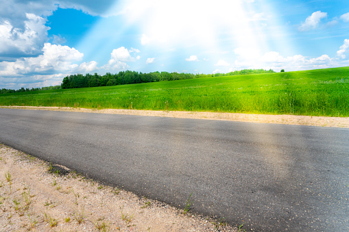 Road along the green field and sunbeams like sun rays. The concept of good mood and positivity. Landscape shot