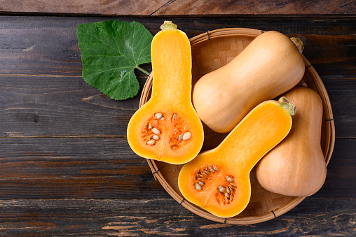 Half a butternut roasted on a baking tray with rosemary on a grey background