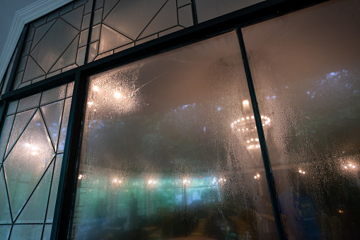 A rotunda with glass windows all around, decorated for an event, is fogged on a rainy day. The lights set up for an event to come are shining through the haze of fog.