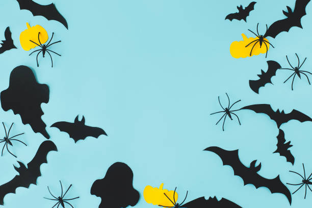 istock Halloween flat lay. Black ghosts, spiders, bats and yellow pumpkins decorations on blue background flat lay. Happy Halloween! Card template with space for text. Modern minimal frame 1427445353